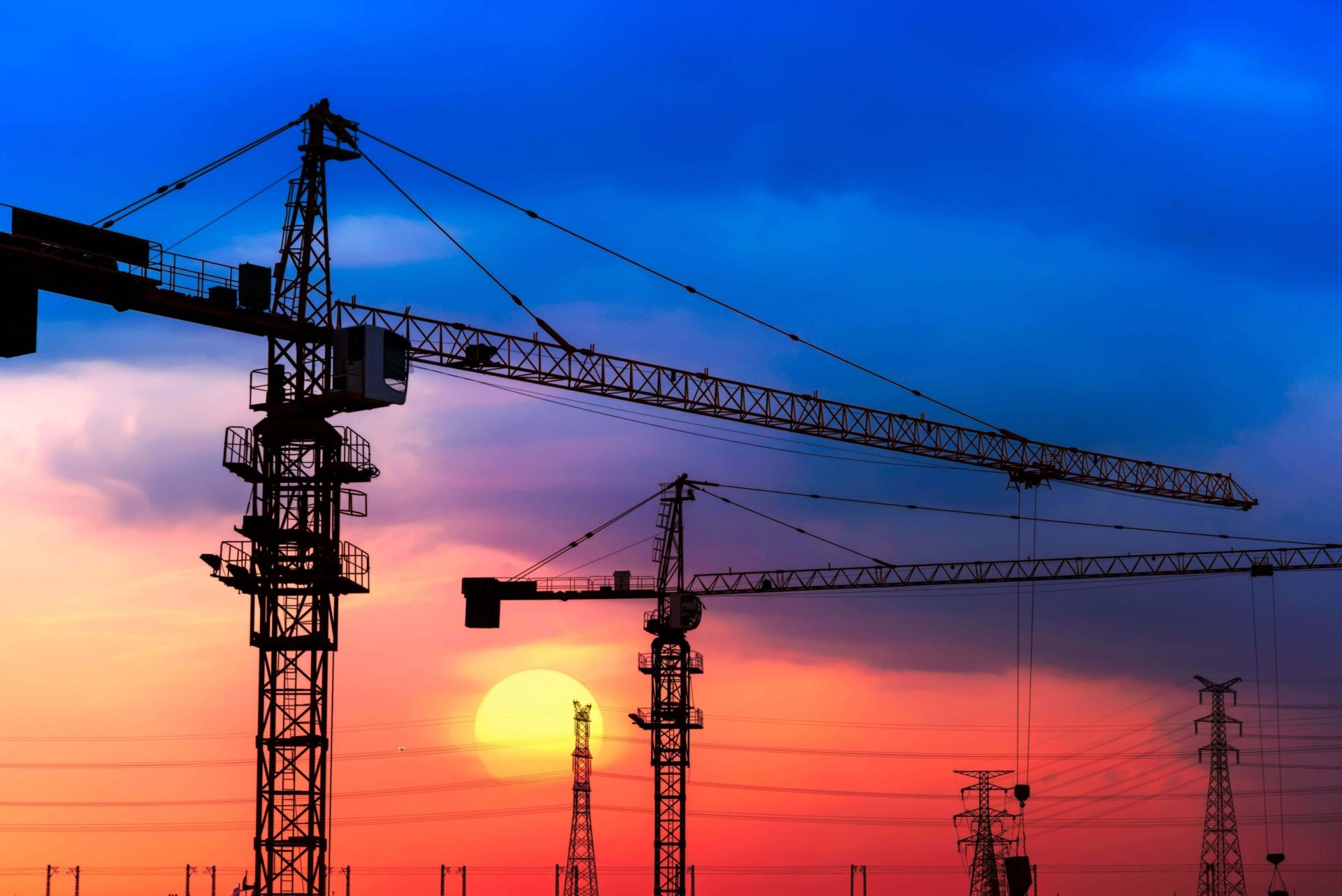 Industrial construction cranes and building silhouettes over sun